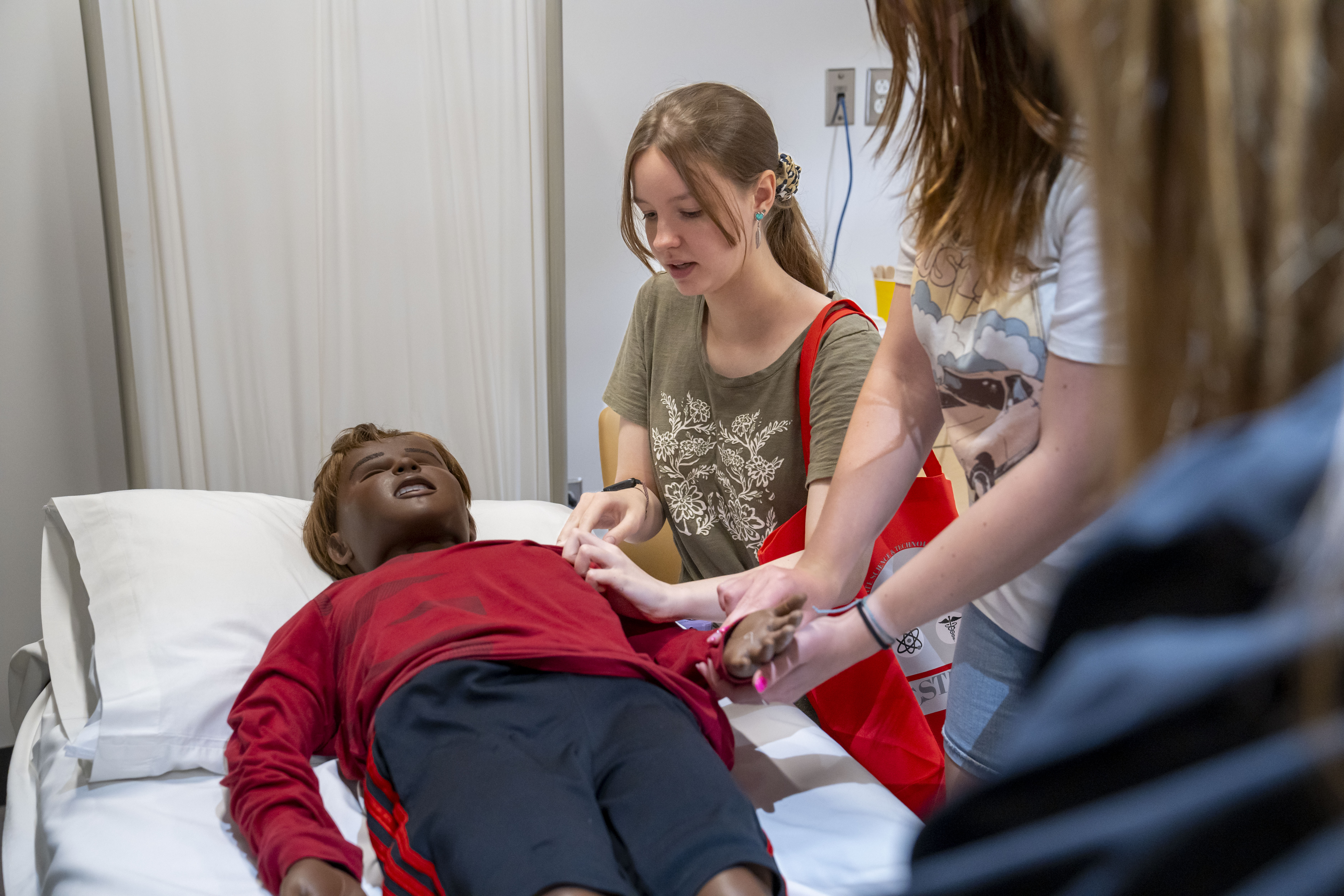 Three students taking a manikin's pulse inside the Simulation Center at the Health Professions Hub at D'Youville University