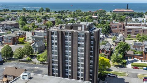 in the foreground you see a 12 story brown rectangular building, in the distance you see Lake Erie.