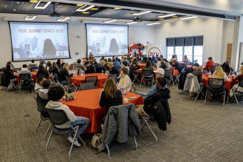 large room filled with round tables. people sit around the tables looking at presentation at the front of the room