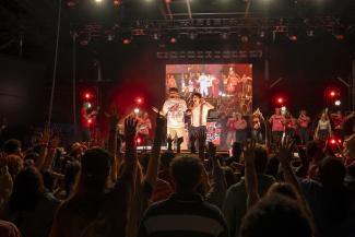 a group of people stand on a concert stage in front of a crowd