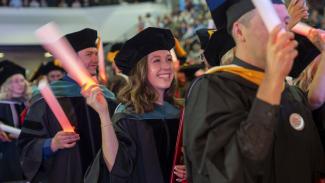 students in regalia and tams wave light up batons in celebration at a commencement ceremony.