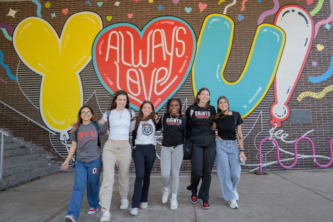 six students walking arm in arm in front of a mural. The mural reads: Always Love You!
