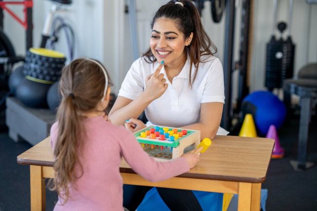 Young woman points to the shape of her mouth while a young child watches