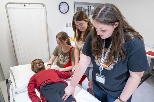 Three students check the pulse of a manikin in the Health Professions Hub at D'Youville