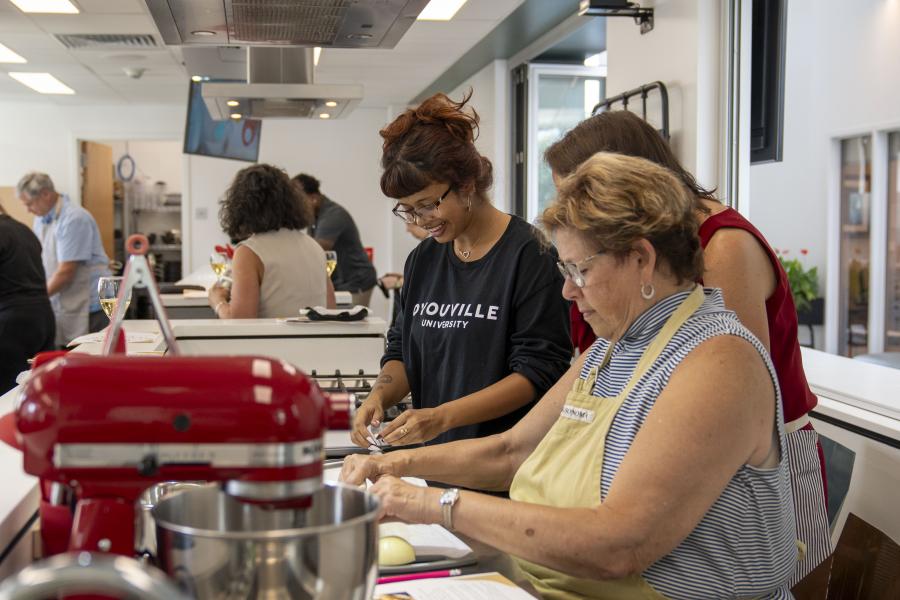 a group of women gathered at a cooking station within a multi-station kitchen