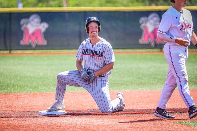 D'Youville University baseball player kneels on third base at ECC Championship final game.