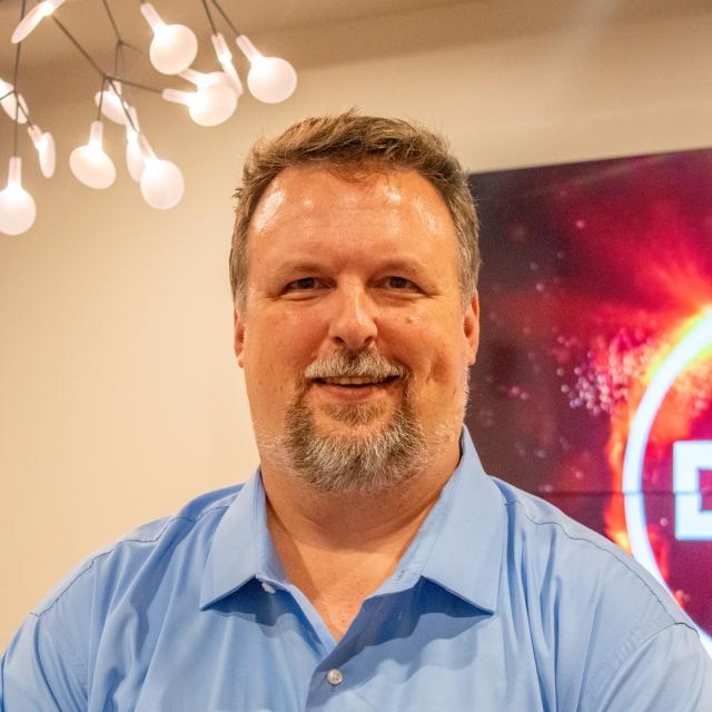 man in blue shirt stands smiling at the camera.